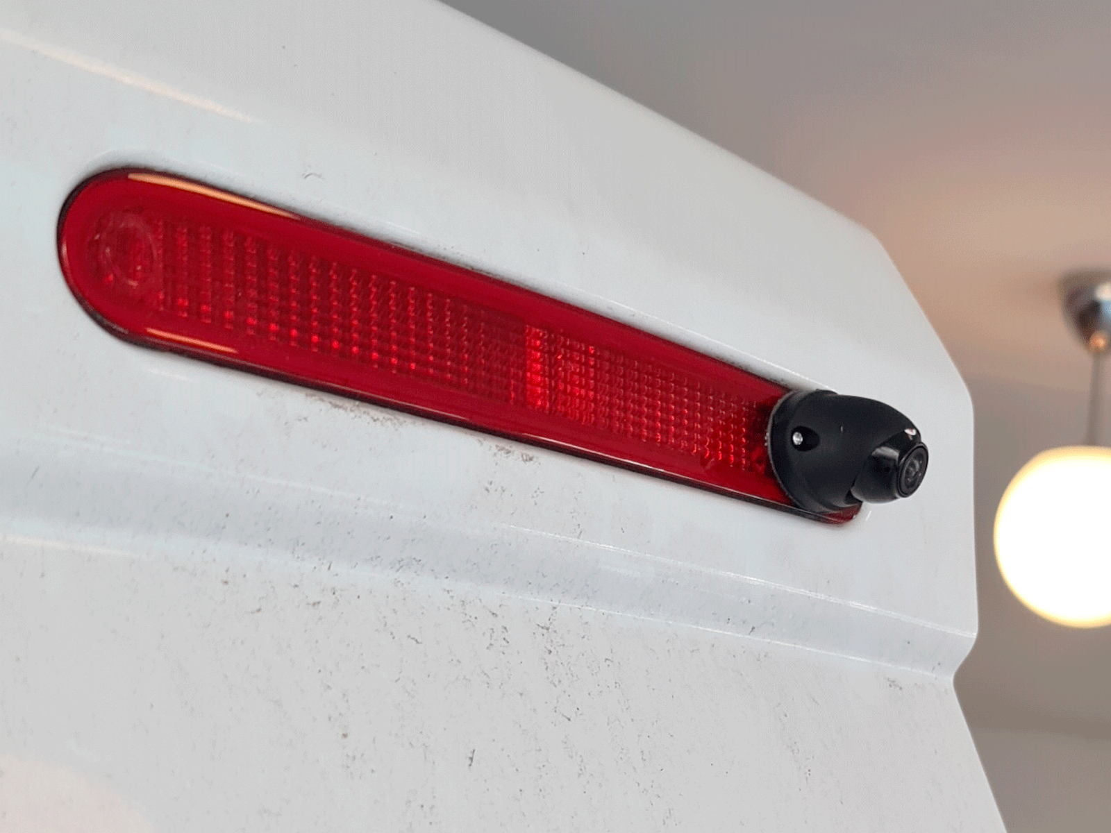 3040007_4_3040007_4.png Red horizontal tail light on a white vehicle with a small backup camera at the end, near the bumper edge
